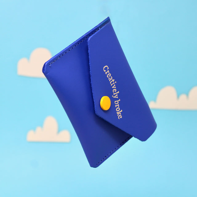 A royal blue purse with 'Creatively broke' embossed on the outside