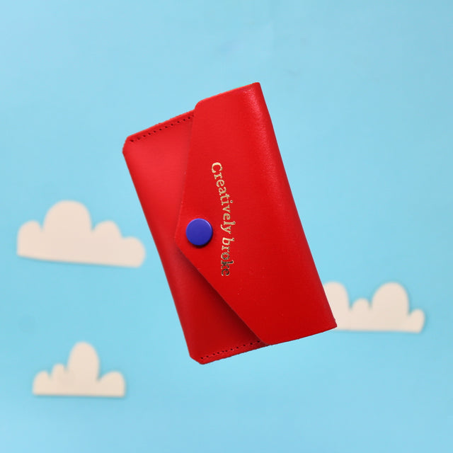 A red leather purse with 'Creatively broke' embossed on the outside
