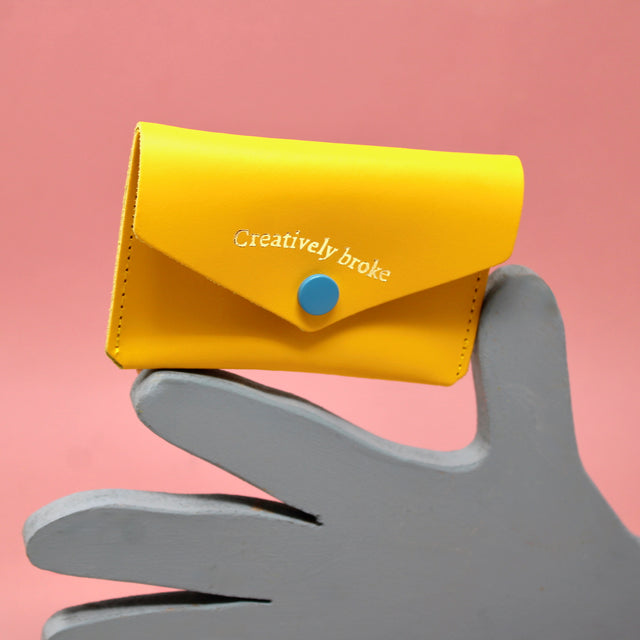 Yellow leather wallet with 'Creatively broke' embossed on the front